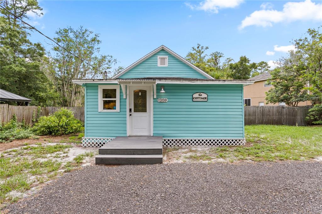 A light blue cottage with white trim, a small wooden deck, and a gravel driveway — 1209 QUINTUPLET COURT, CASSELBERRY, FL