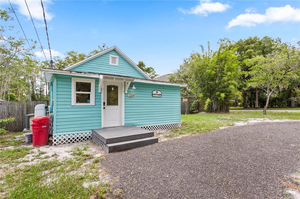 A light blue cottage with horizontal siding features a small wooden deck and red trash bin — 1209 QUINTUPLET COURT, CASSELBERRY, FL