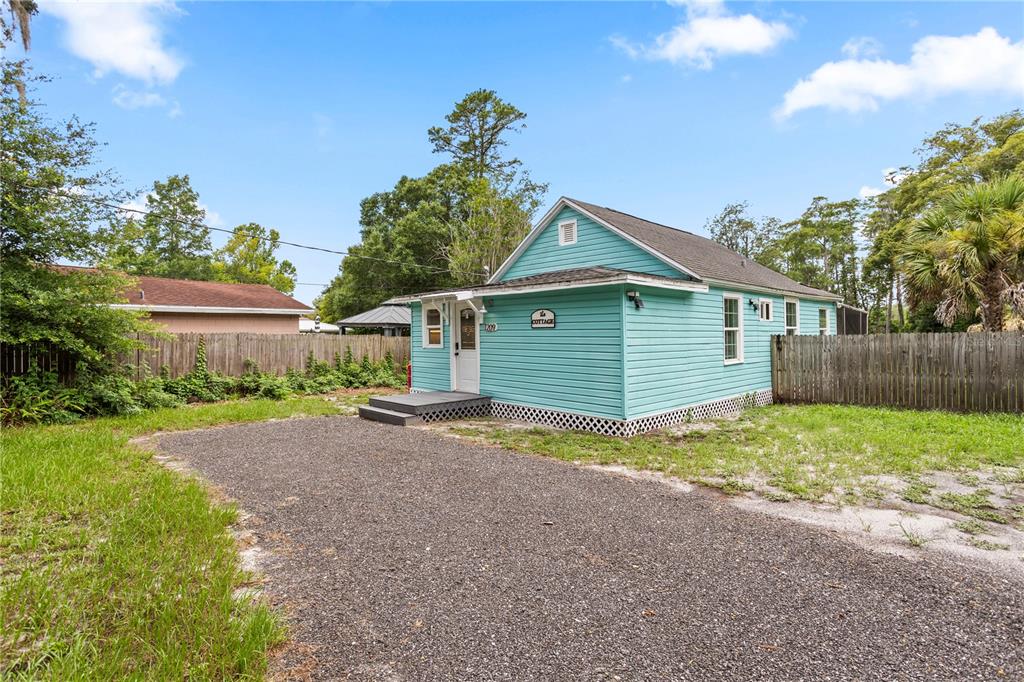 A light blue cottage with a gravel driveway and a wooden fence in the yard — 1209 QUINTUPLET COURT, CASSELBERRY, FL