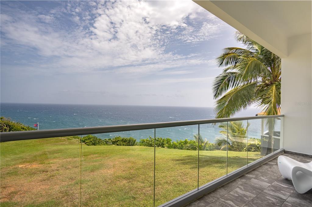 A balcony with a glass railing overlooks a grassy lawn and the ocean — 991 CALLE ESTACION, QUEBRADILLAS, PR