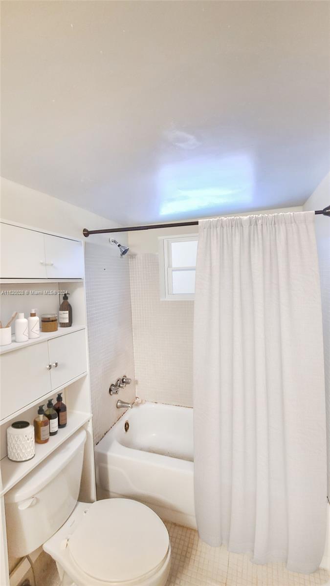 A bathroom features a white bathtub, a shower curtain, a toilet, and built-in wall shelving — 7410 SW 82nd St # K211, Miami FL 33143, MIAMI, FL