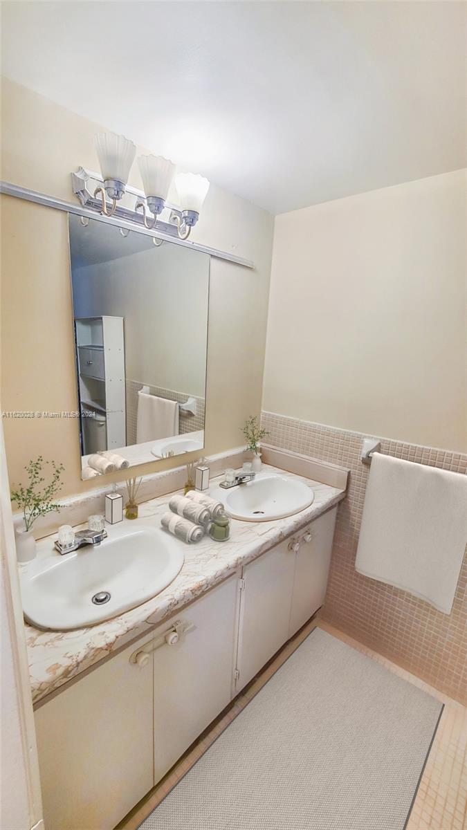 A bathroom features a double vanity with white cabinets, marble-look countertops, and a wall-mounted mirror — 7410 SW 82nd St # K211, Miami FL 33143, MIAMI, FL