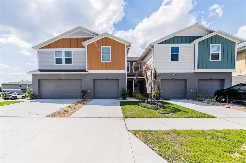 A two-story duplex building features four garage doors and contrasting gray, orange, and teal siding — 4345 HILLOCK BOULEVARD, HAINES CITY, FL