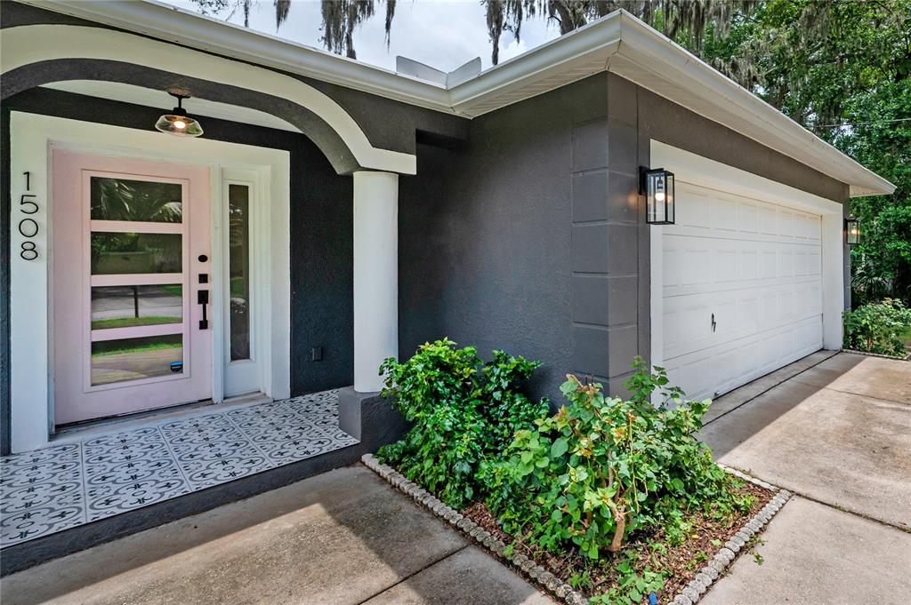 A house exterior features a pink front door, patterned tile porch, and a white garage — 1508 E JEAN STREET, TAMPA, FL