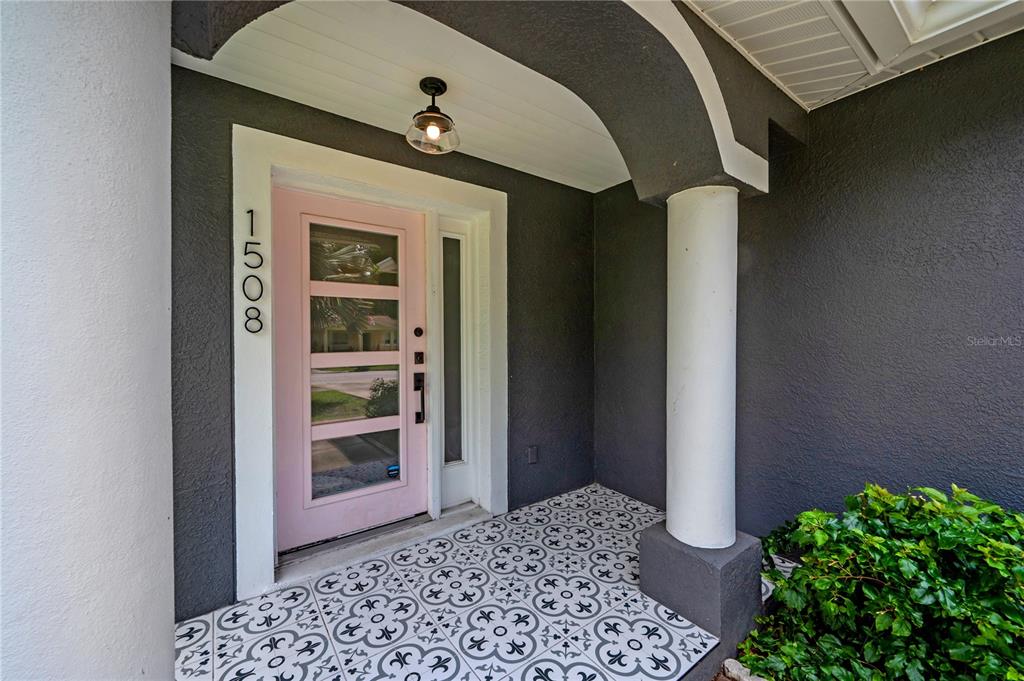 A front porch features a pink door, patterned tile flooring, and a white column — 1508 E JEAN STREET, TAMPA, FL