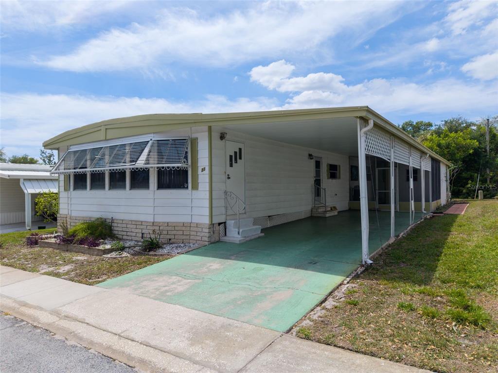A single-story mobile home with a green carport and a white exterior — 23 MOUNTAIN LAUREL DRIVE, PALM HARBOR, FL
