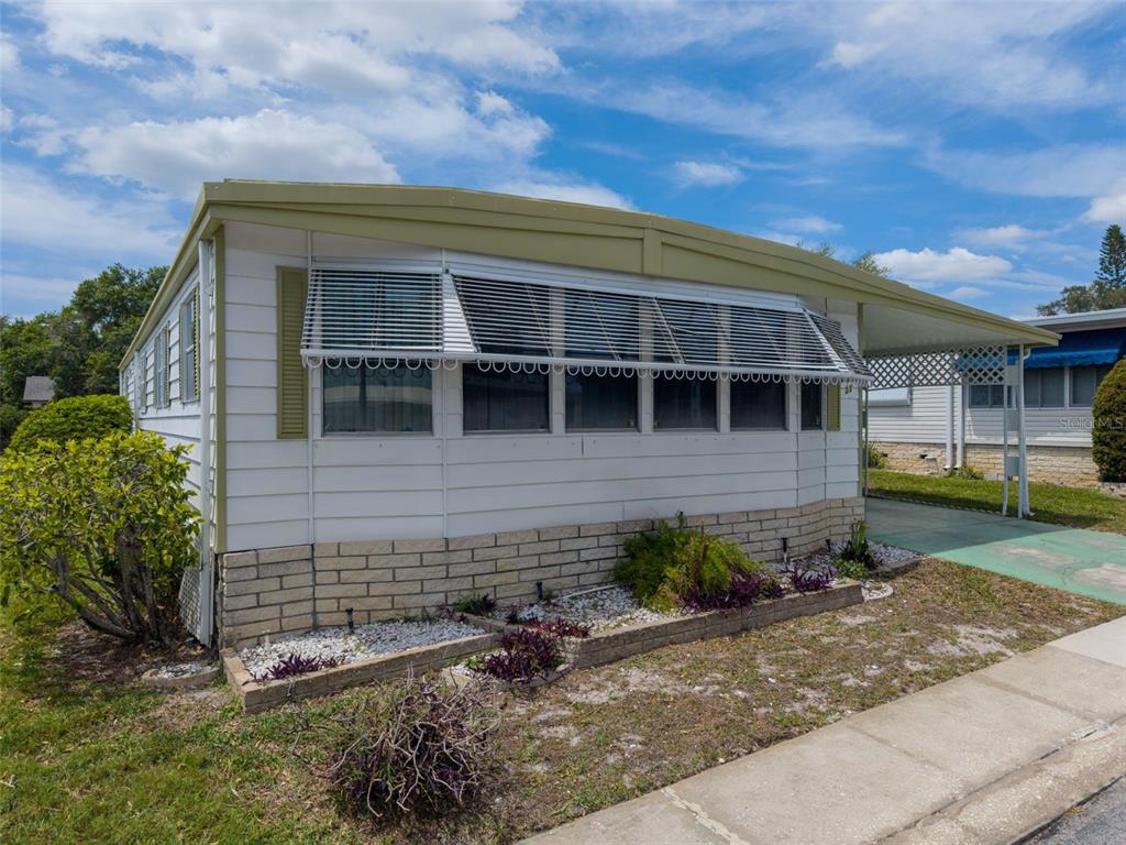 A single-story mobile home with white siding, a brick base, and a metal carport — 23 MOUNTAIN LAUREL DRIVE, PALM HARBOR, FL