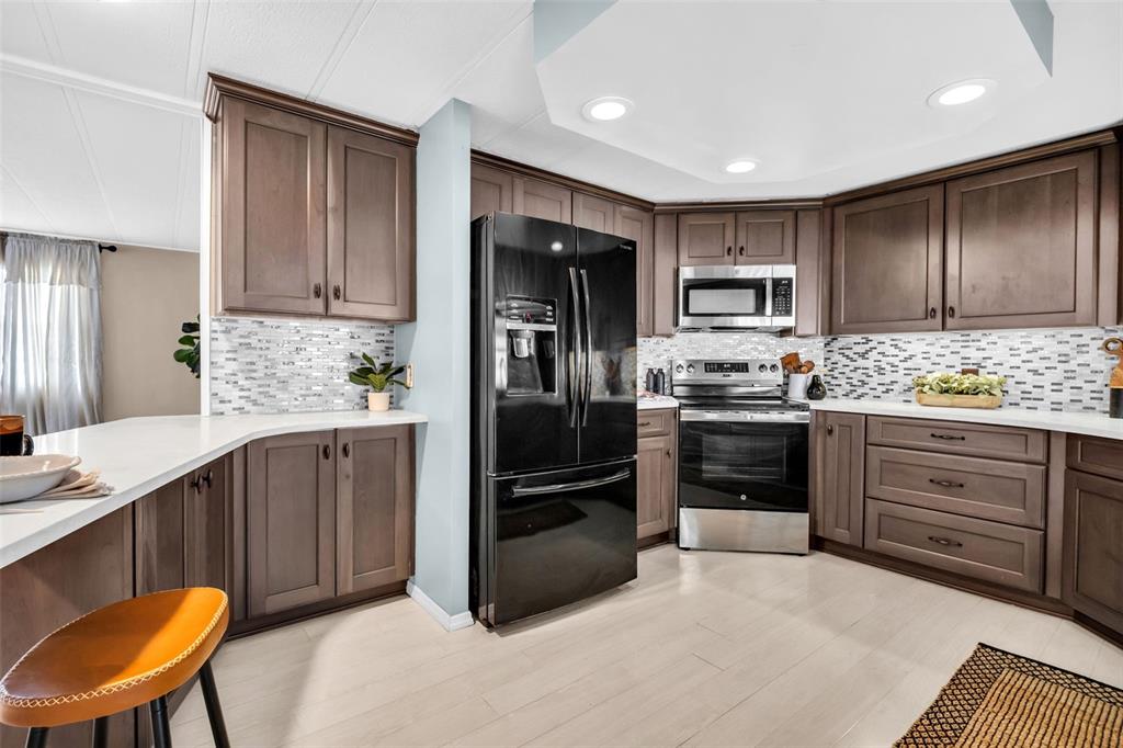 A kitchen features dark wood cabinets, stainless steel appliances, a black refrigerator, and tile backsplash — 23 MOUNTAIN LAUREL DRIVE, PALM HARBOR, FL