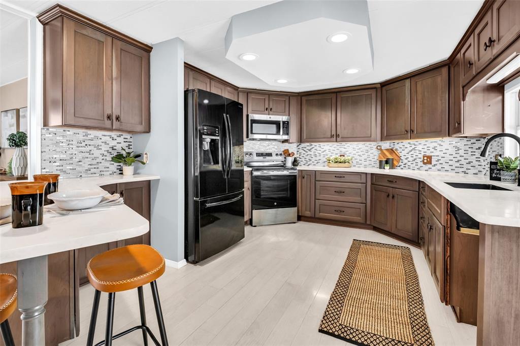 A kitchen features brown cabinets, stainless steel appliances, white countertops, and a mosaic tile backsplash — 23 MOUNTAIN LAUREL DRIVE, PALM HARBOR, FL