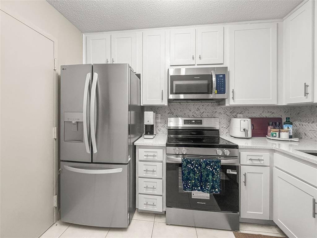 A kitchen with white cabinets, stainless steel appliances, and a patterned tile backsplash — 2700 BAYSHORE BOULEVARD UNIT 2110, DUNEDIN, FL