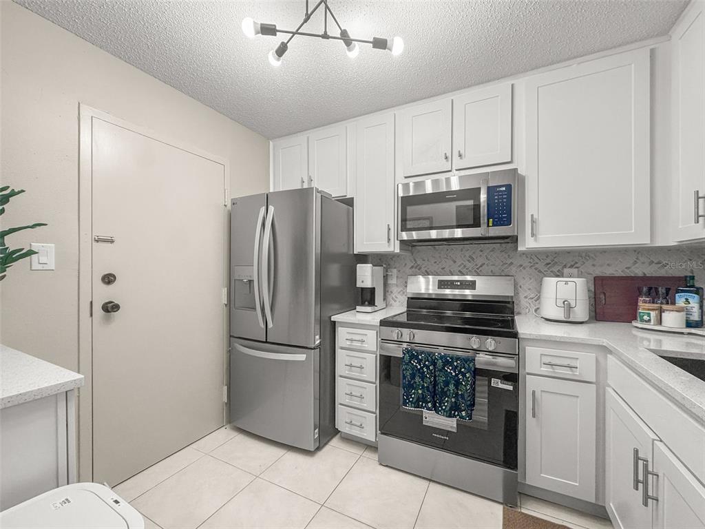 A kitchen features white cabinets, stainless steel appliances, and light-colored tile flooring — 2700 BAYSHORE BOULEVARD UNIT 2110, DUNEDIN, FL
