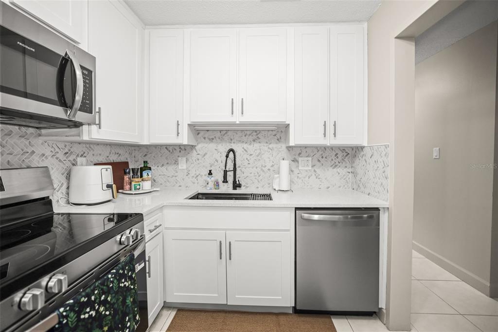 A kitchen features white cabinets, stainless steel appliances, a herringbone backsplash, and a dark faucet — 2700 BAYSHORE BOULEVARD UNIT 2110, DUNEDIN, FL