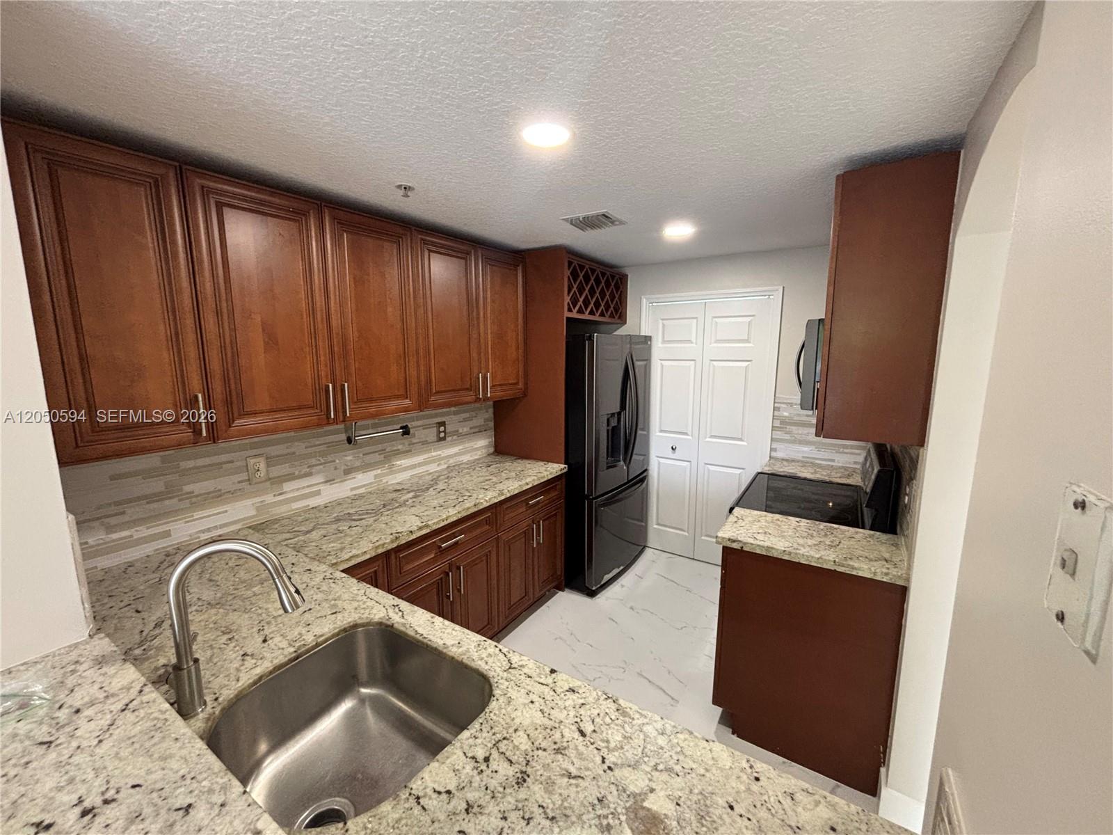 A kitchen features dark wood cabinets, granite countertops, stainless steel appliances, and a tile backsplash — 6440 NW 114th Ave # 424, Doral FL 33178, DORAL, FL