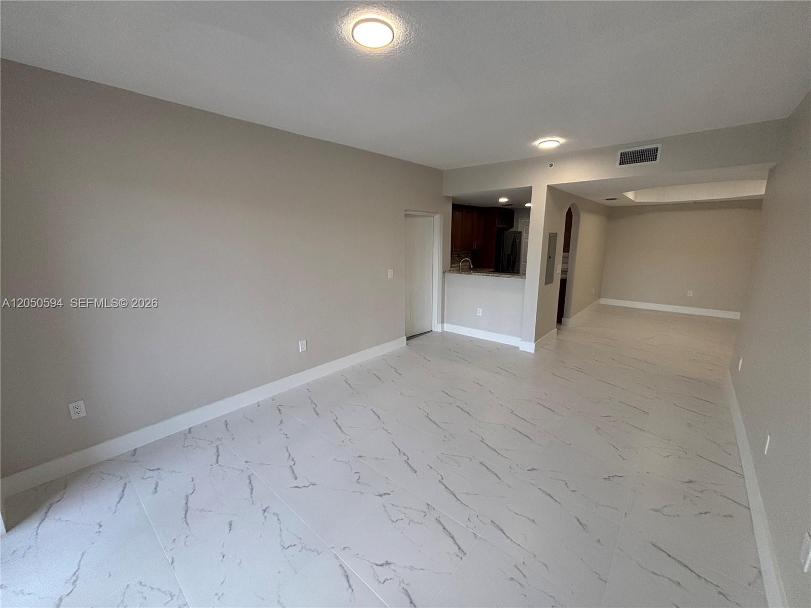 An empty room features light-colored walls, white marble-patterned tile flooring, and a small kitchen area — 6440 NW 114th Ave # 424, Doral FL 33178, DORAL, FL