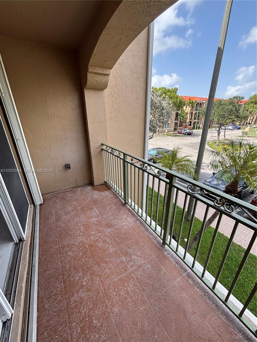 A balcony with reddish-brown tiled flooring and a green metal railing overlooks a parking lot — 6440 NW 114th Ave # 424, Doral FL 33178, DORAL, FL