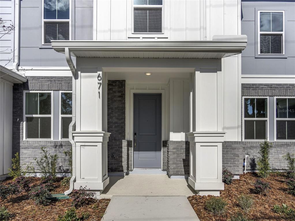 The exterior of a modern townhome features a gray door, white columns, and brick accents — 671 CLARK STREET, OVIEDO, FL