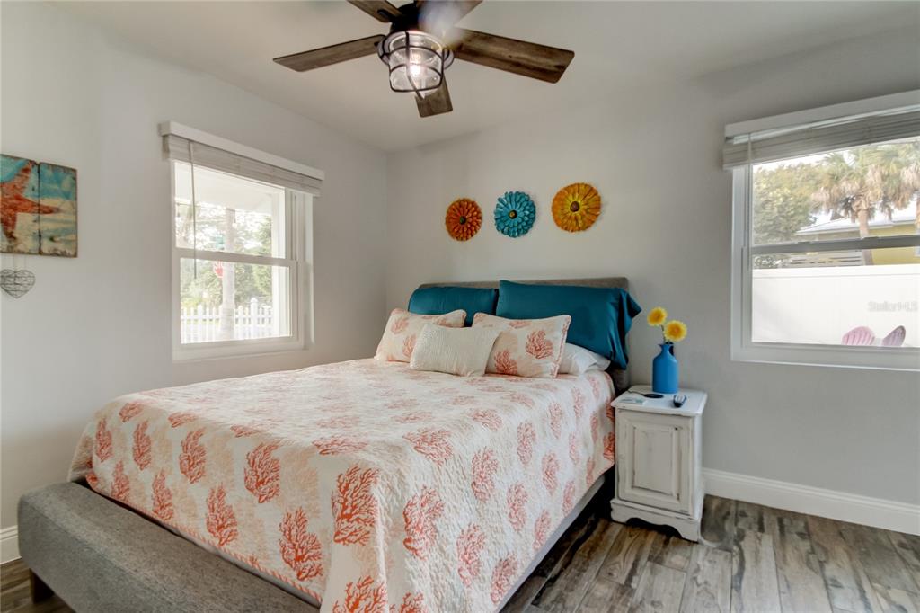 A bedroom features a bed with coral-patterned bedding, a ceiling fan, and two windows — 1907 2ND STREET, INDIAN ROCKS BEACH, FL