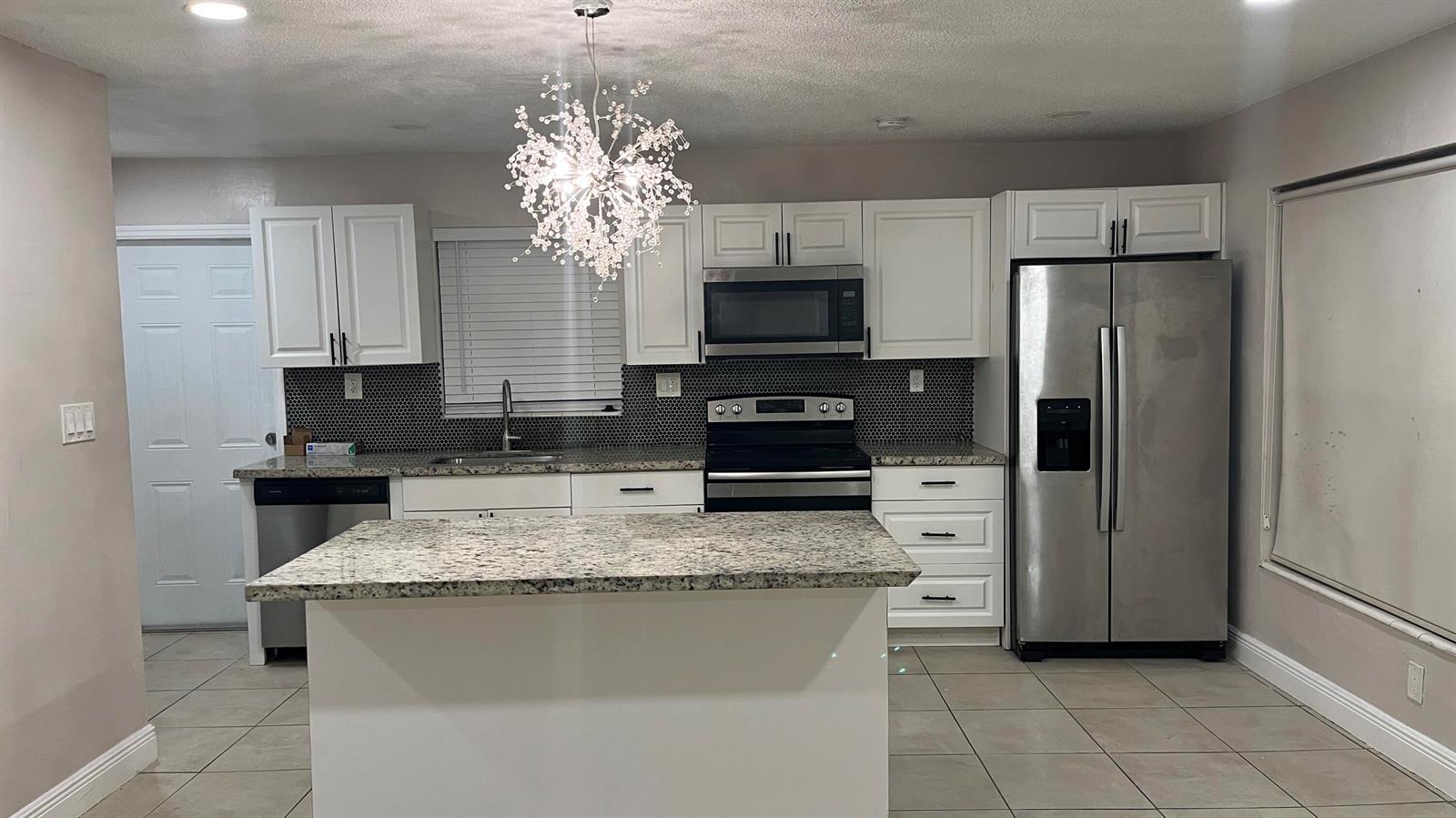 A kitchen features white cabinets, granite countertops, stainless steel appliances, and a modern crystal chandelier — 2001 NE 2nd Terrace, Pompano Beach FL 33060, POMPANO BEACH, FL