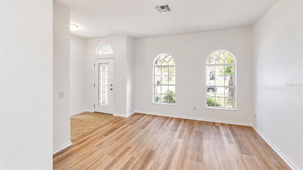 An empty room with light wood-look flooring, two arched windows, and a front entryway — 30612 PALMERSTON PLACE, WESLEY CHAPEL, FL