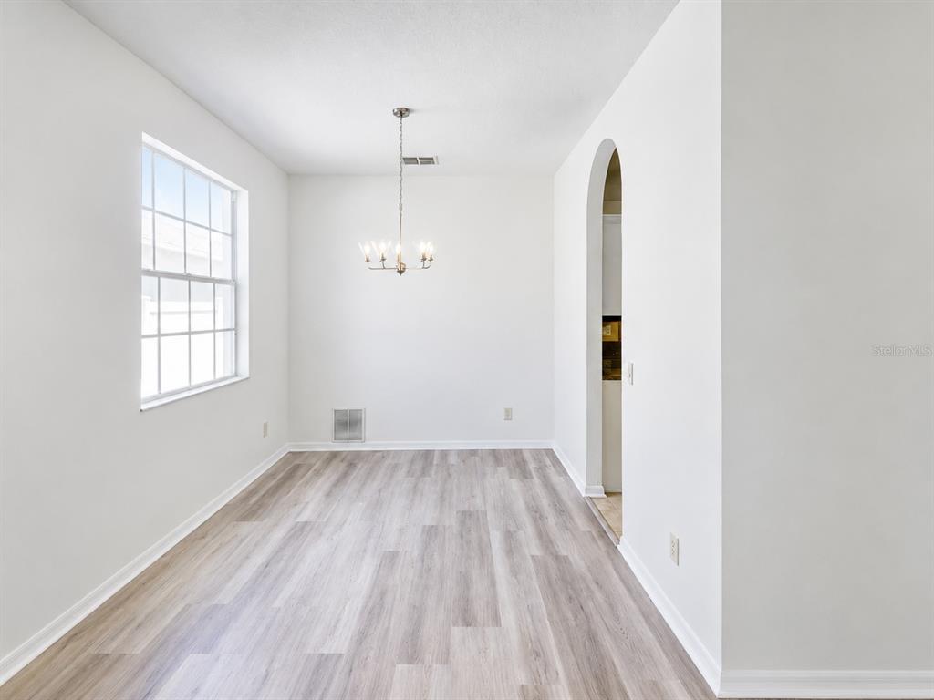 A dining room with white walls, light wood-look flooring, a chandelier, and an arched doorway — 30612 PALMERSTON PLACE, WESLEY CHAPEL, FL