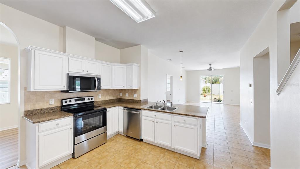 A kitchen with white cabinets, stainless steel appliances, and granite countertops opens to a living area — 30612 PALMERSTON PLACE, WESLEY CHAPEL, FL
