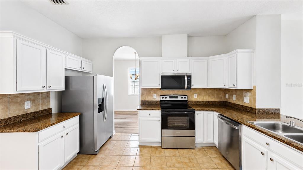 A kitchen features white cabinets, granite countertops, stainless steel appliances, and tile flooring — 30612 PALMERSTON PLACE, WESLEY CHAPEL, FL