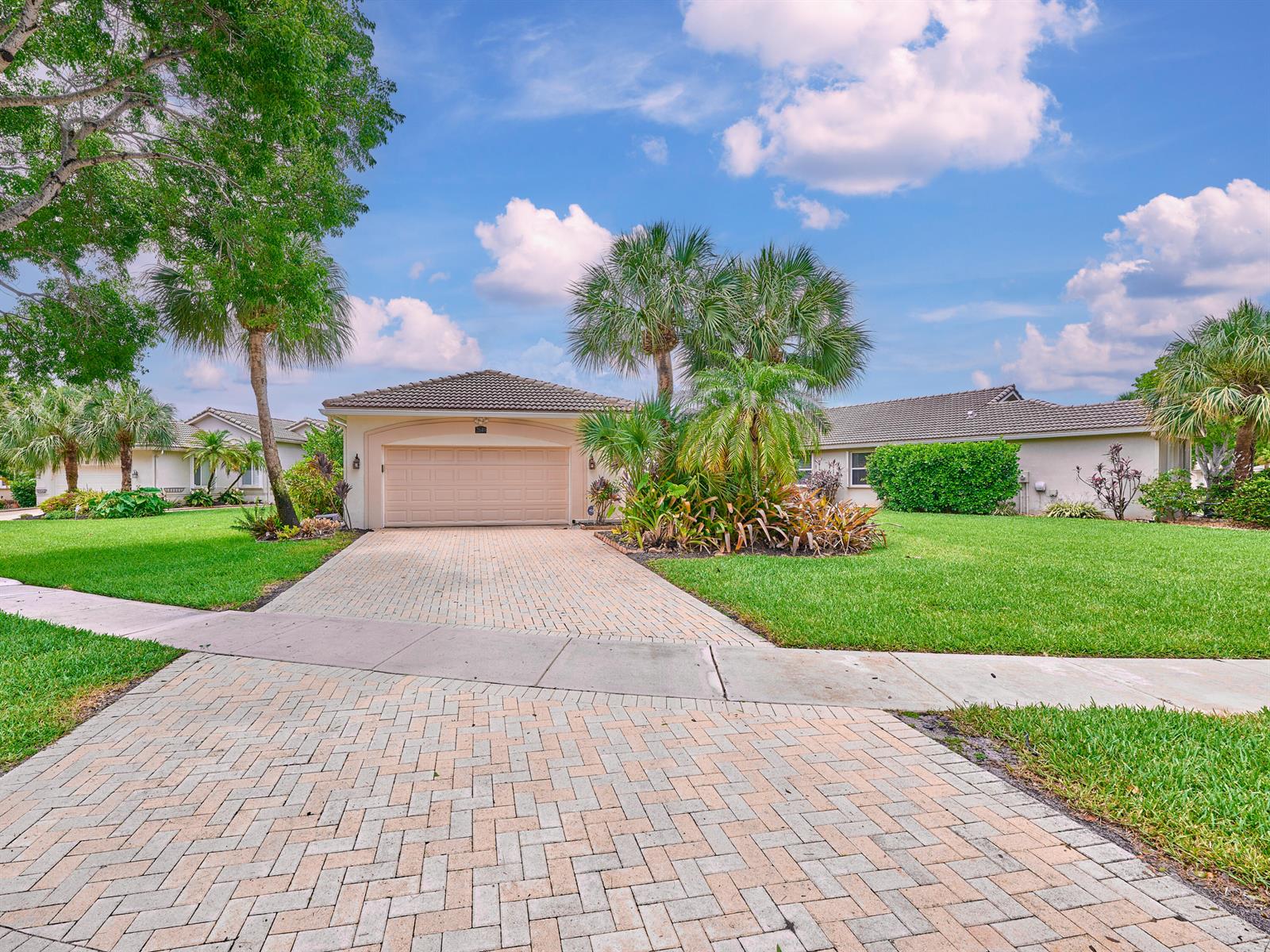 A single-story house with a beige garage, paver driveway, and palm trees under a blue sky — 2649 Clipper Circle, West Palm Beach FL 33411, WEST PALM BEACH, FL