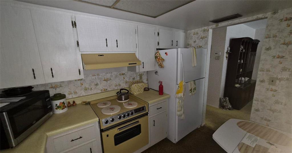 A kitchen features white cabinets, a yellow stove and range hood, and floral wallpaper — 2204 ORANGE BLOSSOM LANE, BRADENTON, FL