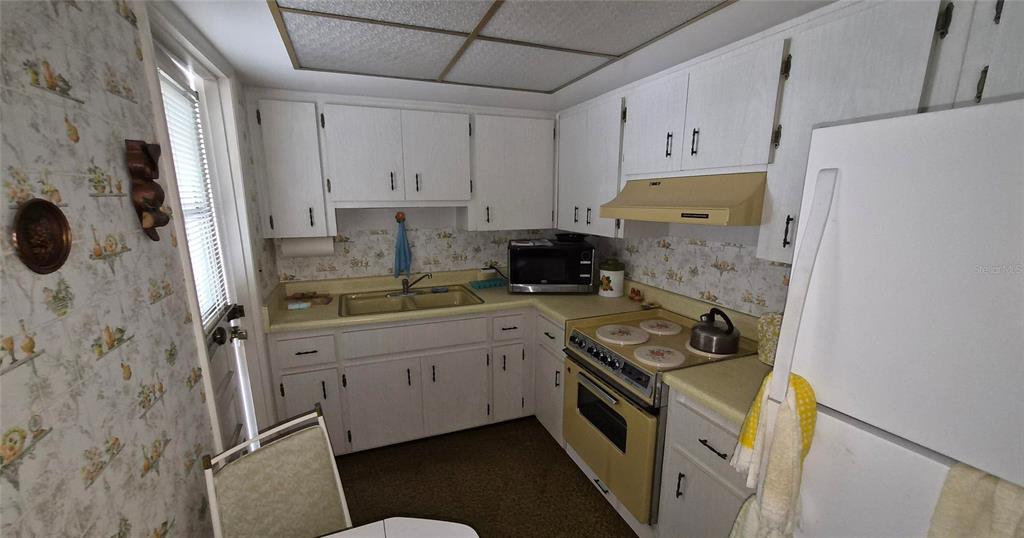 A kitchen features white cabinets, yellow appliances, floral wallpaper, and a drop ceiling — 2204 ORANGE BLOSSOM LANE, BRADENTON, FL
