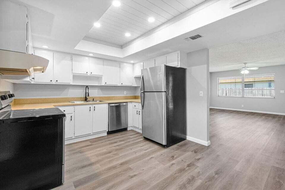 A kitchen with white cabinets, stainless steel appliances, and wood-look flooring opens to a room — 9046 E Highland Pines Boulevard E, Palm Beach Gardens FL 33418, PALM BEACH GARDENS, FL