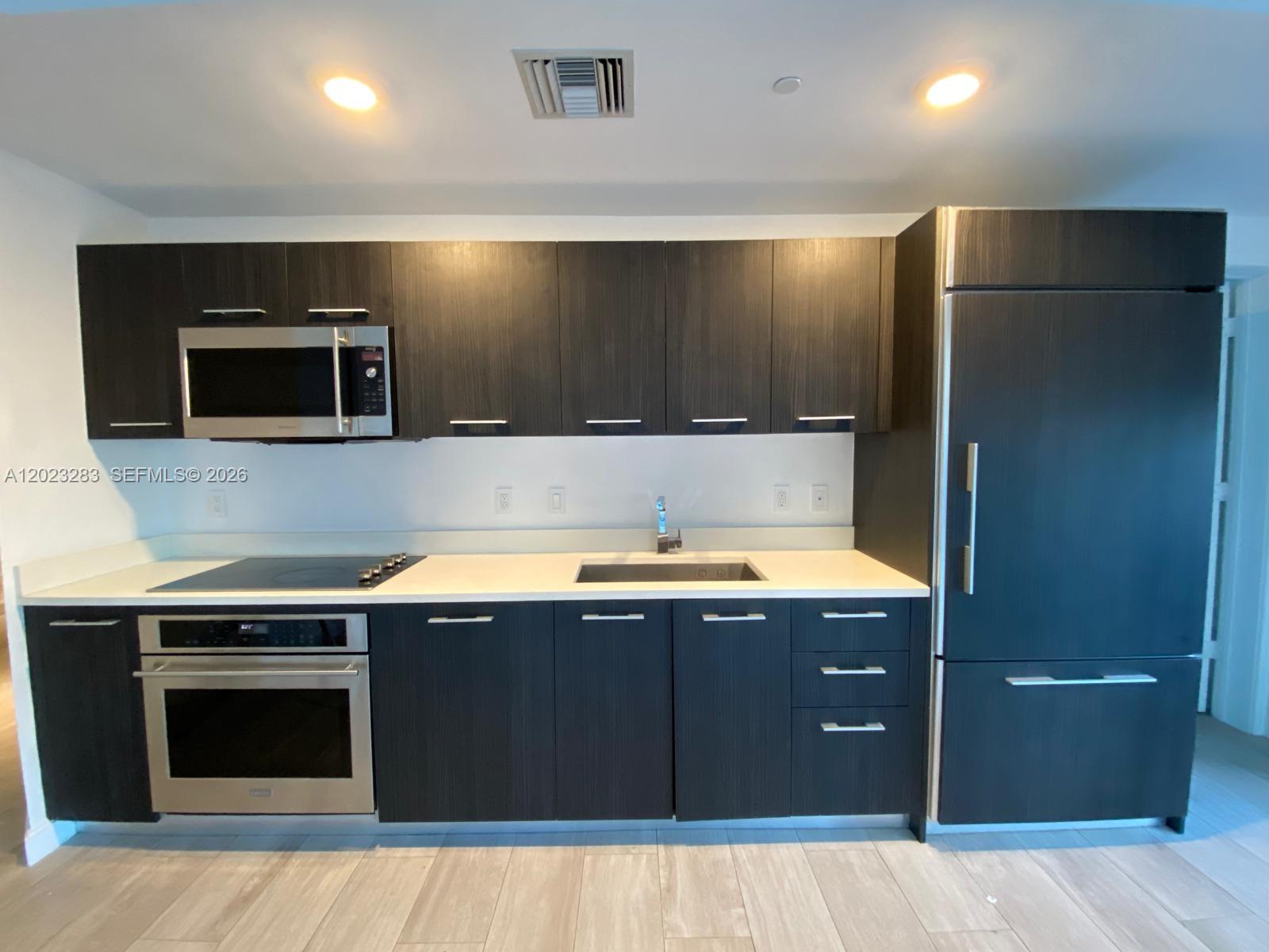 A modern kitchen features dark wood cabinets, stainless steel appliances, and white countertops — 55 SW 9th St # 1503, Miami FL 33130, MIAMI, FL