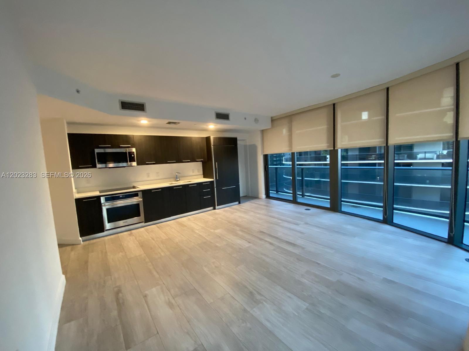 A modern kitchen with dark cabinetry and stainless steel appliances opens into a living area — 55 SW 9th St # 1503, Miami FL 33130, MIAMI, FL