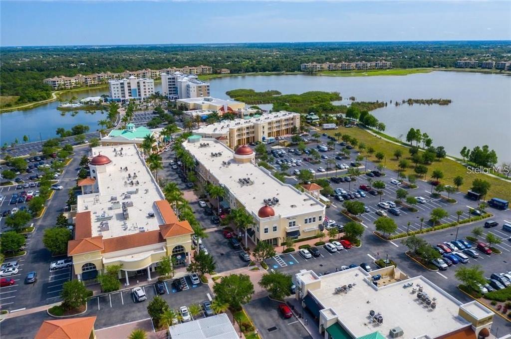 An aerial view shows a commercial shopping complex with parking lots situated beside a large lake — 8111 LAKEWOOD MAIN STREET UNIT 307, LAKEWOOD RANCH, FL
