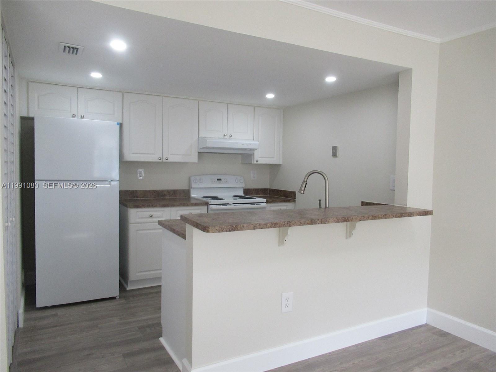 A kitchen features white cabinets, a white refrigerator, and a brown countertop breakfast bar — 6825 SW 45th Ln # 12, Miami FL 33155, MIAMI, FL