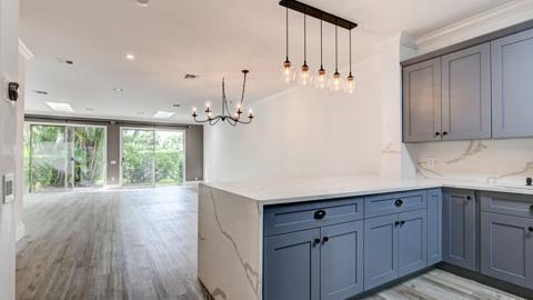 A kitchen with blue cabinets and a marble island overlooks an open living area — 6784 Via Regina, Boca Raton FL 33433, BOCA RATON, FL