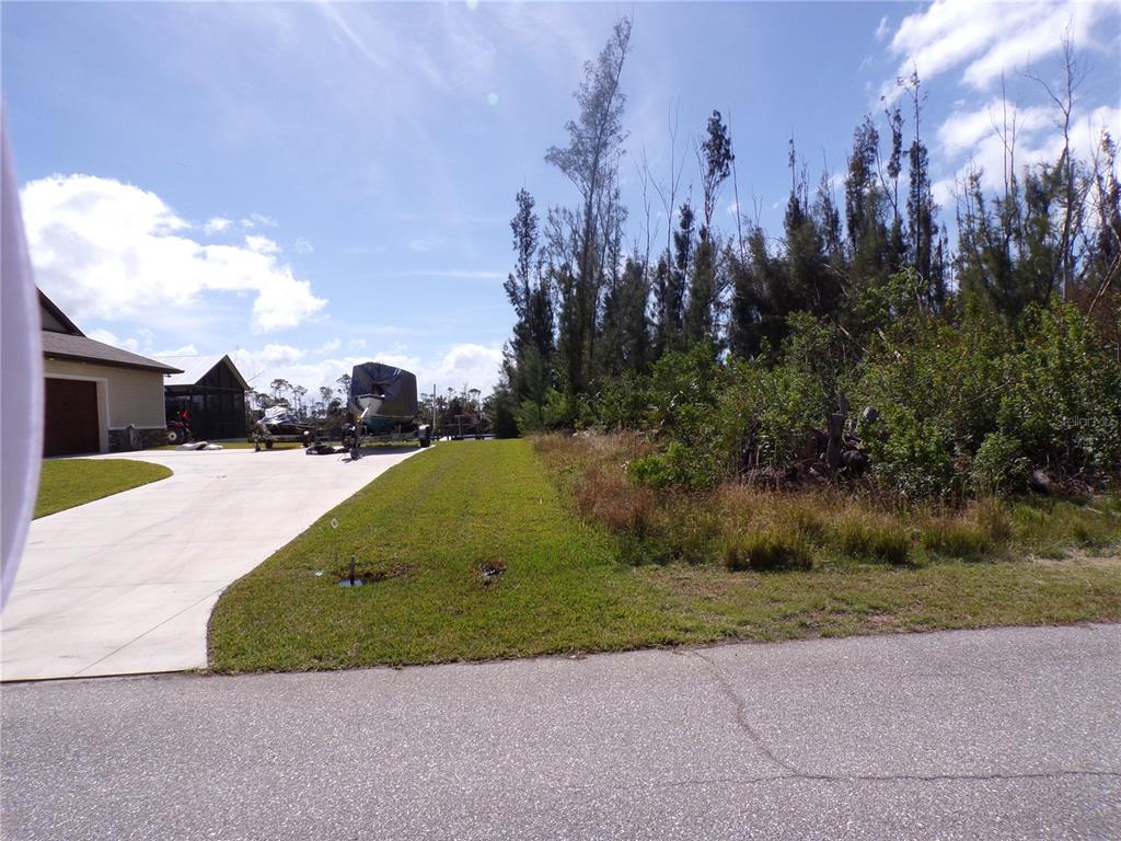 A paved driveway leads to a house next to an undeveloped, wooded lot — 16724 LIGGETT CIRCLE, PORT CHARLOTTE, FL