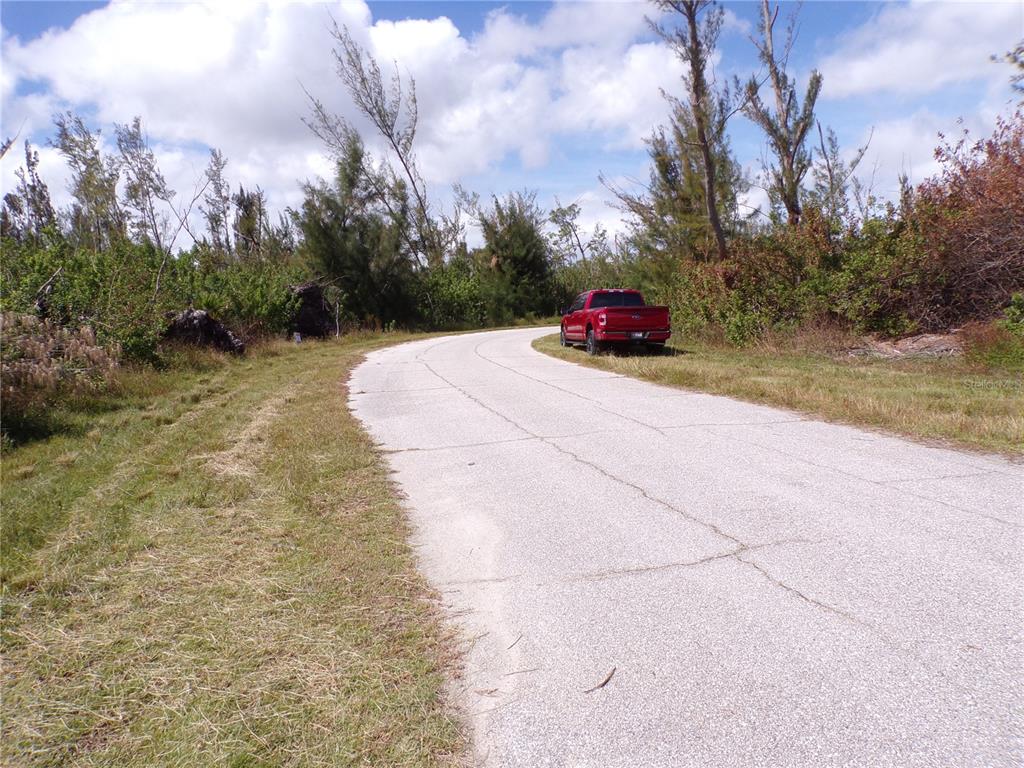 A red pickup truck is parked on the shoulder of a paved, curving rural road — 16724 LIGGETT CIRCLE, PORT CHARLOTTE, FL