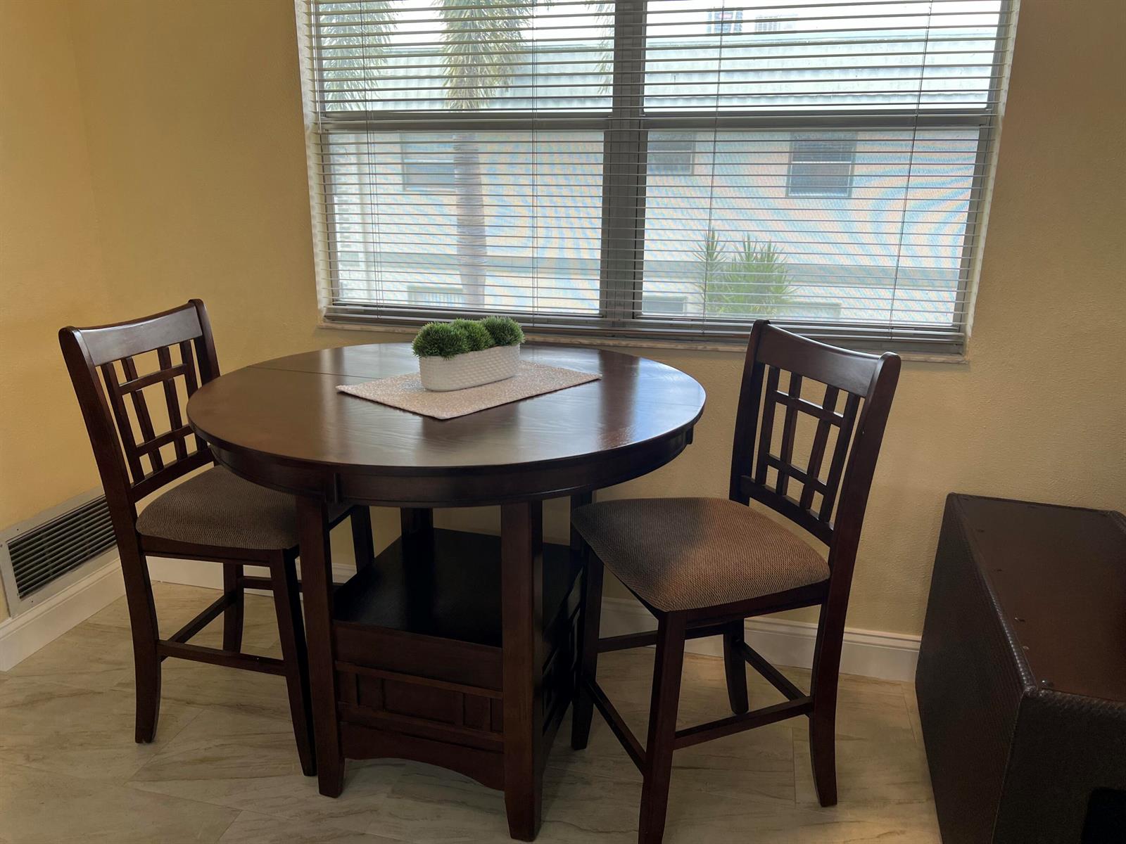 A round wooden dining table with two chairs sits in front of a window — 711 Monaco Court, Delray Beach FL 33446, DELRAY BEACH, FL