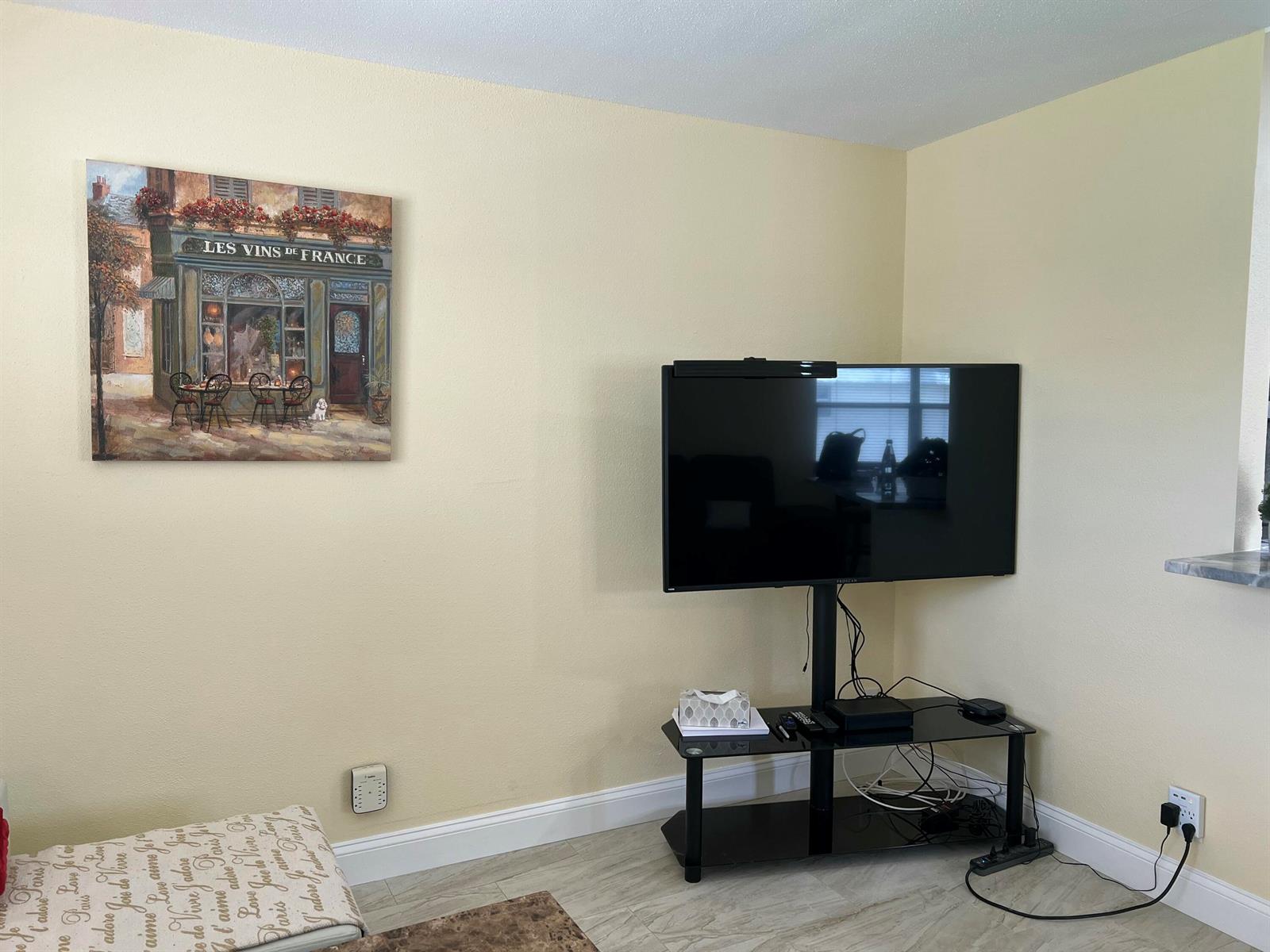 A living room wall features a French-themed painting, a flat-screen television on a stand, and flooring — 711 Monaco Court, Delray Beach FL 33446, DELRAY BEACH, FL