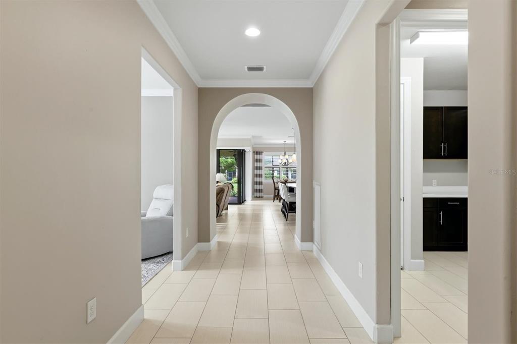 A hallway with light tile flooring leads through an arched doorway toward a dining area — 16932 PELHAM PLACE, LAKEWOOD RANCH, FL