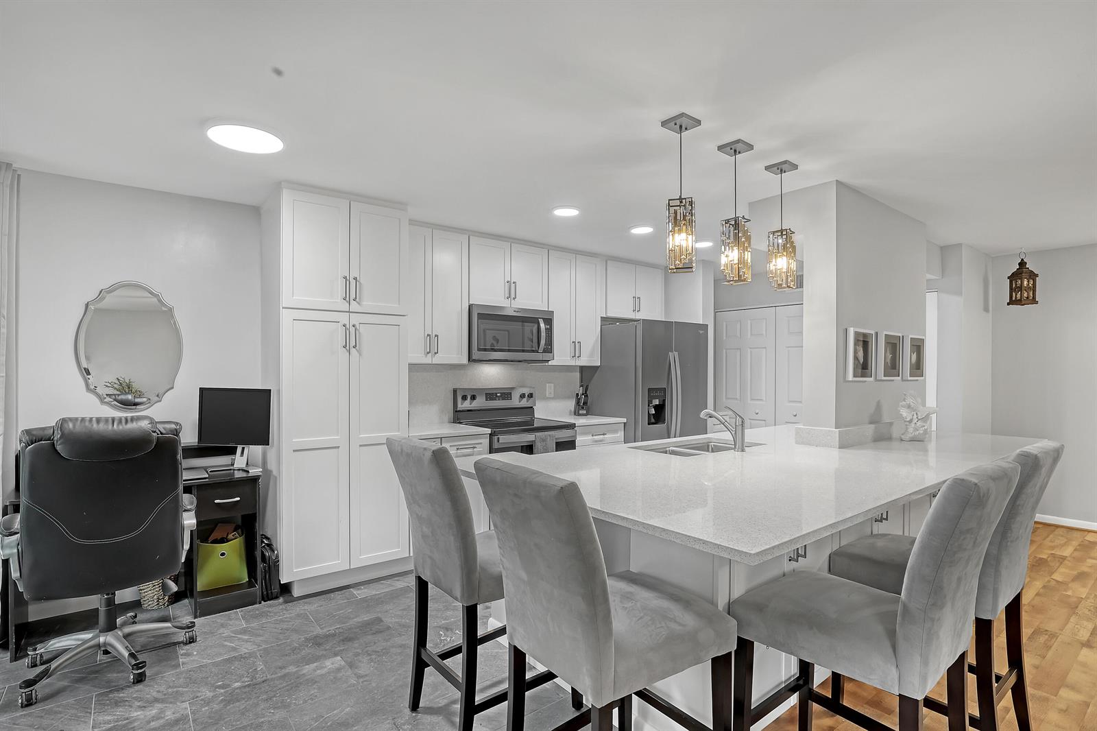 A kitchen features white cabinetry, a large quartz island with grey stools, and a desk area — 105 Half Moon Circle # F1, Hypoluxo FL 33462, HYPOLUXO, FL