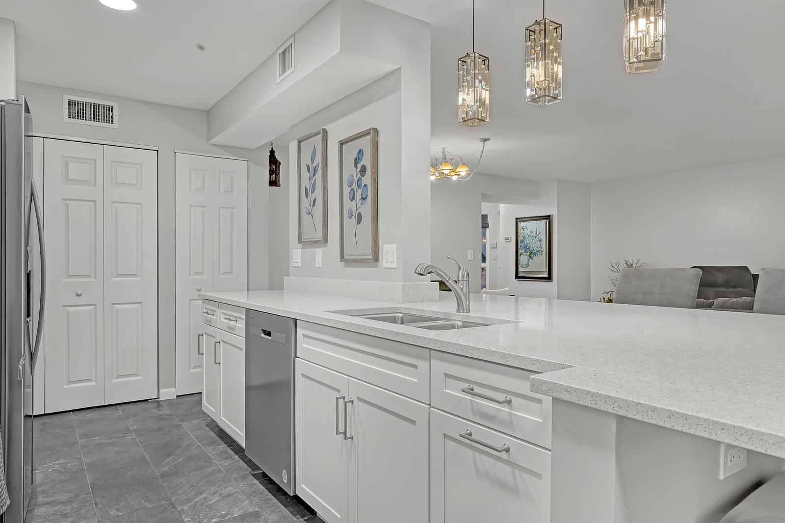A modern kitchen features white cabinets, quartz countertops, stainless steel appliances, and pendant lighting — 105 Half Moon Circle # F1, Hypoluxo FL 33462, HYPOLUXO, FL