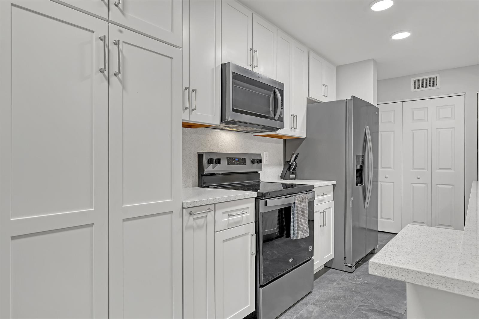 A kitchen features white cabinets, stainless steel appliances, and gray tile flooring — 105 Half Moon Circle # F1, Hypoluxo FL 33462, HYPOLUXO, FL