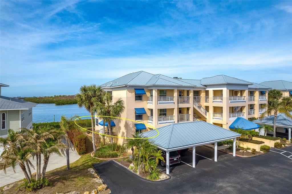 An exterior view of a multi-story apartment building with a yellow facade and blue awnings — 2424 PLACIDA ROAD UNIT C101, ENGLEWOOD, FL