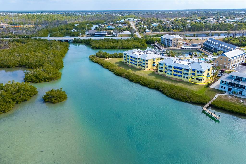 An aerial view shows a multi-story yellow apartment building situated along a coastal waterway — 2424 PLACIDA ROAD UNIT C101, ENGLEWOOD, FL