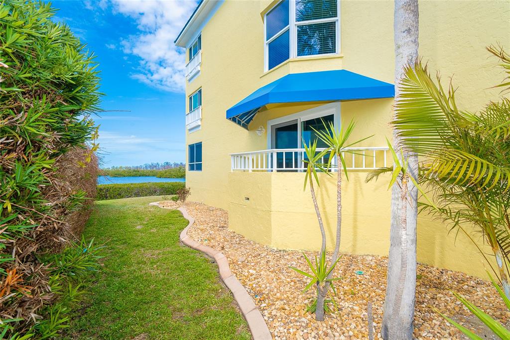 A yellow multi-story building exterior features a blue awning over a ground-floor patio door — 2424 PLACIDA ROAD UNIT C101, ENGLEWOOD, FL