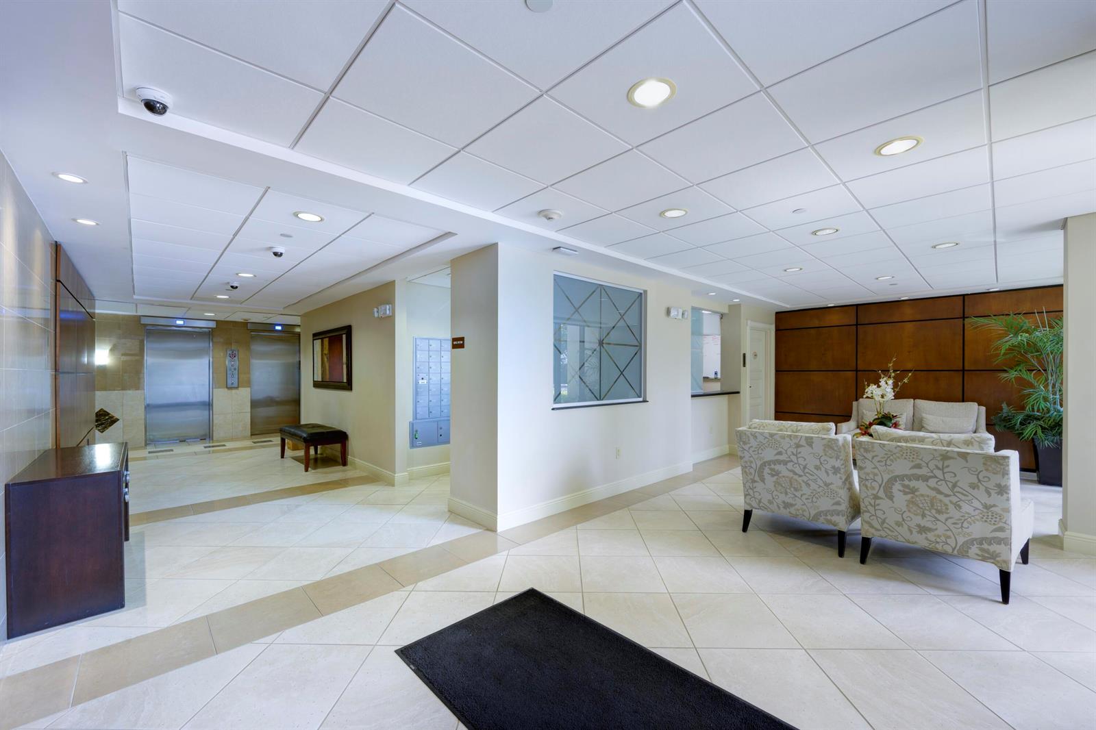 A modern building lobby features tiled floors, a seating area, elevators, and a mail station — 4200 N Ocean Drive # 405, Singer Island FL 33404, SINGER ISLAND, FL