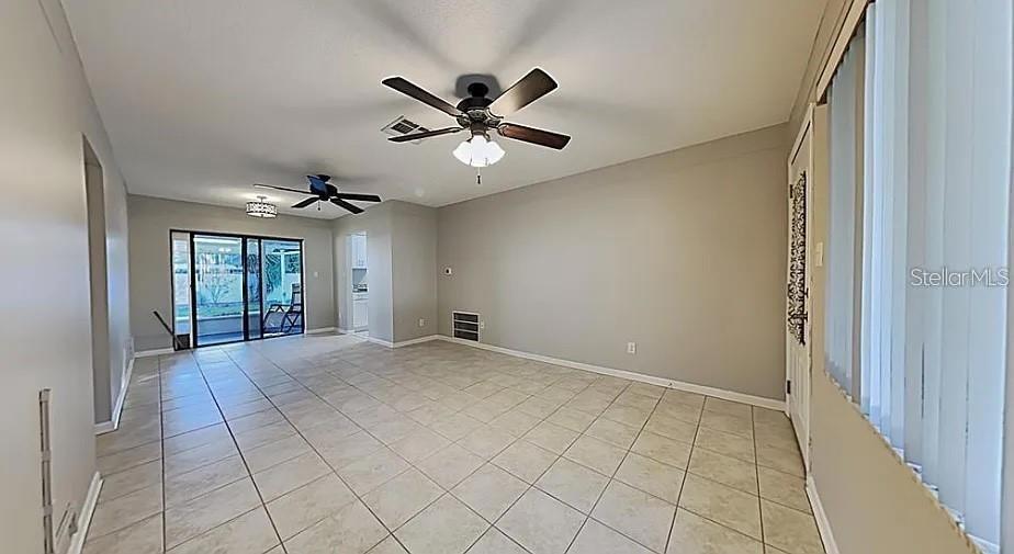 An empty room features light-colored tile flooring, two ceiling fans, and sliding glass patio doors — 7481 OAK STREET NE, ST PETERSBURG, FL