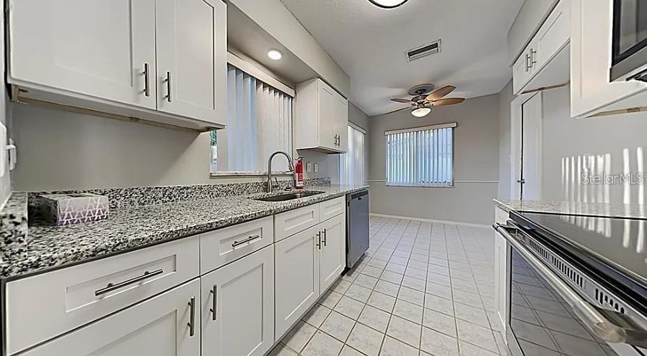 A kitchen features white cabinets, granite countertops, a ceiling fan, and tiled flooring — 7481 OAK STREET NE, ST PETERSBURG, FL