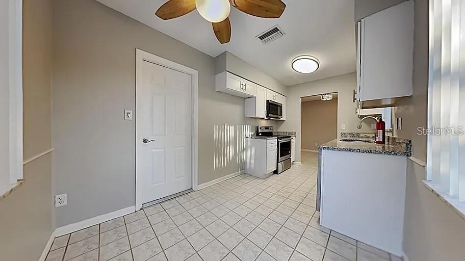 A kitchen features light gray walls, white cabinets, a tiled floor, and a ceiling fan — 7481 OAK STREET NE, ST PETERSBURG, FL